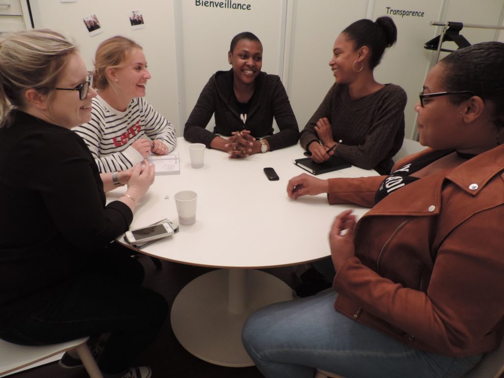 Cinq auxiliaires de vie échangent autour d'une table ronde, sous les mots « Bienveillance » et « Transparence » affichés au mur