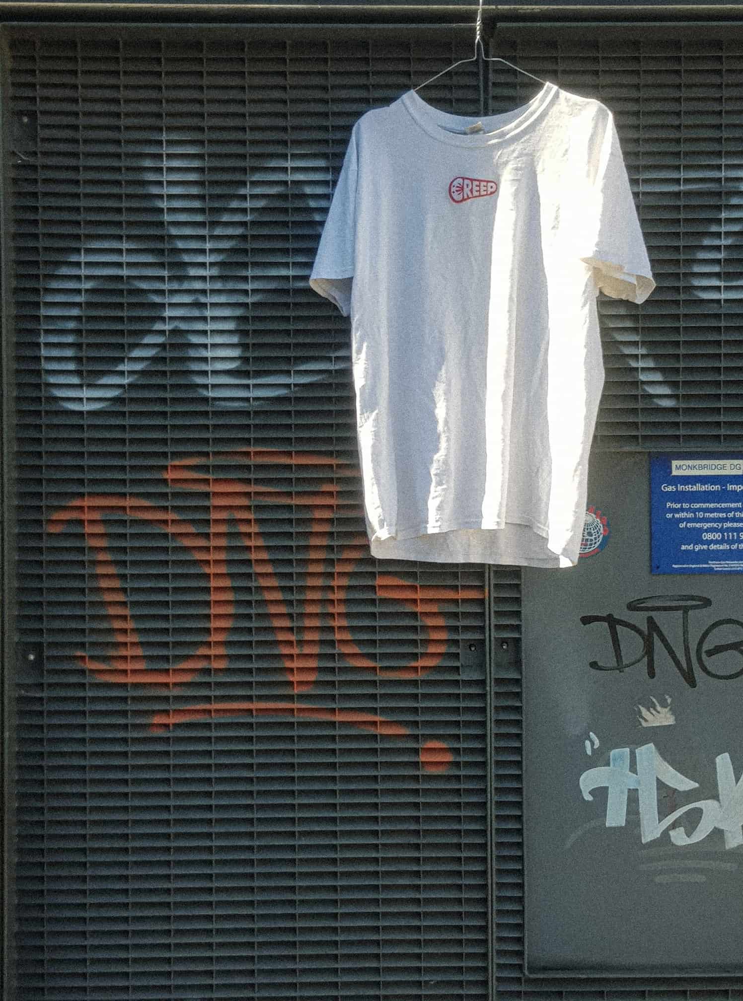 White t-shirt hanging from urban street building with graffiti.