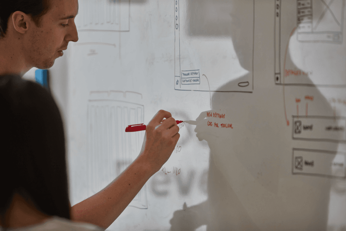 One of the designers writing notes on a whiteboard with wireframes on it