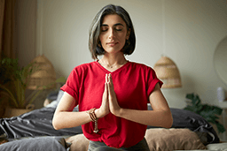 Woman meditating in bedroom with hands in prayer position.