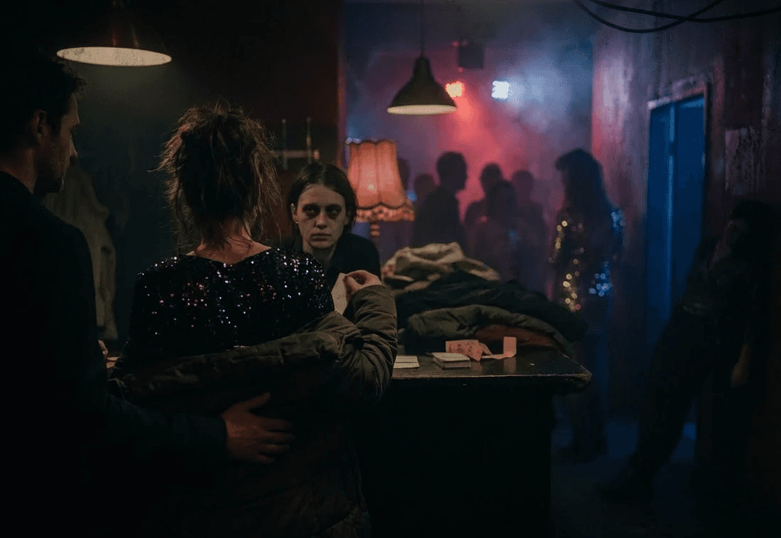A smoky nightclub cloakroom scene where a tired attendant faces a couple wrapped in winter coats, while partygoers shimmer in sequins under dim lamps and colored lights in the hazy background.