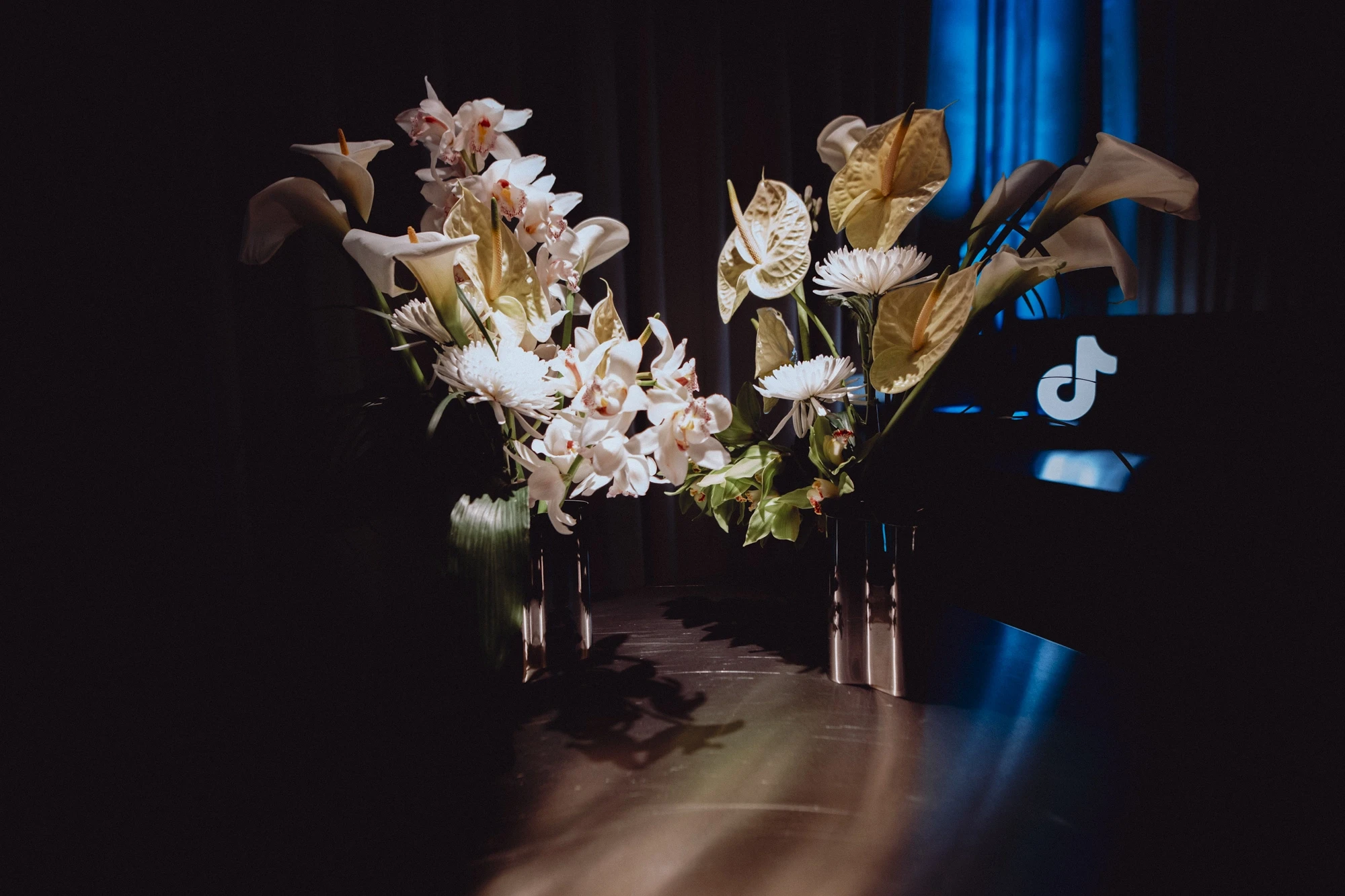White orchids, callas and anthuriums in spotlights next to the glowing TikTok logo.