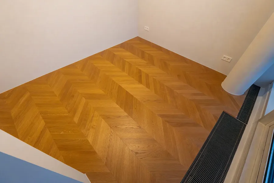 Hochwertiger Chevron-Parkettboden in warmem Holzton in einem modernen Wohnraum mit weißen Wänden.