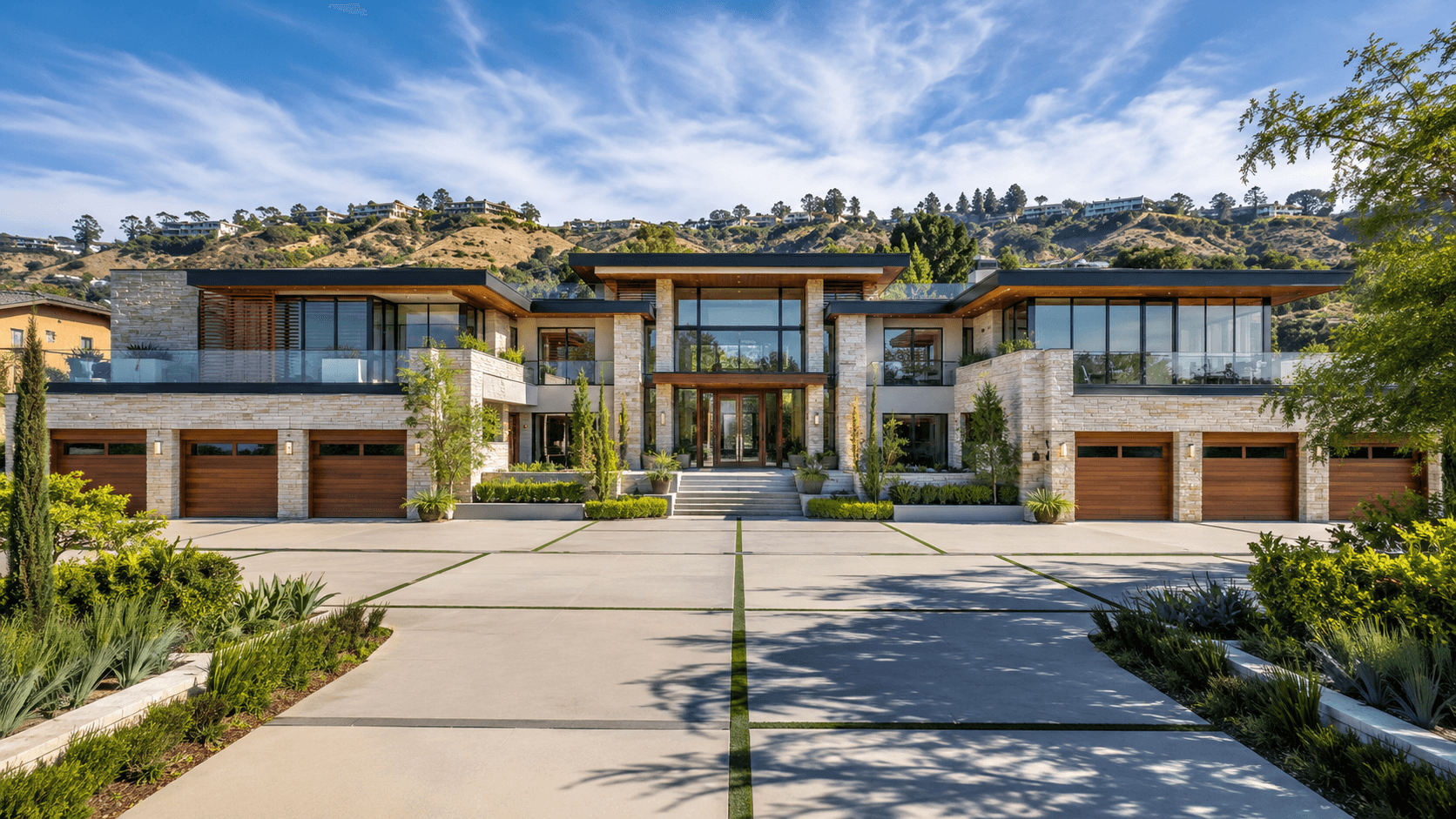 Large modern estate with a stone facade and wide driveway set against rolling hills