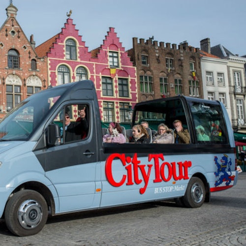 A "City Tour" márkájú városnéző busz, amely utasokat szállít színes történelmi épületek előtt egy macskaköves utcán.