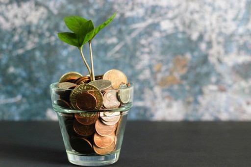 A small plant sprouting from soil in a clear glass jar, sitting on a black surface with a textured background.