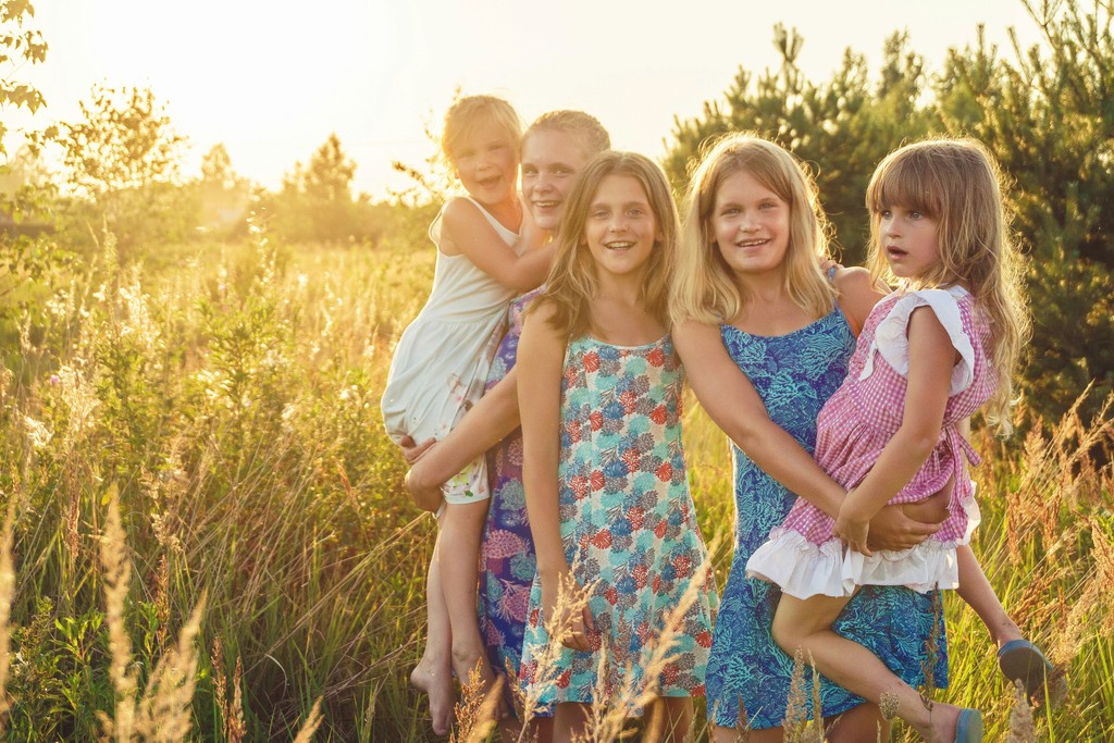 A group of happy children stand together in a sunlit field, wearing colorful summer dresses, capturing the essence of carefree childhood and outdoor fun in a natural setting.