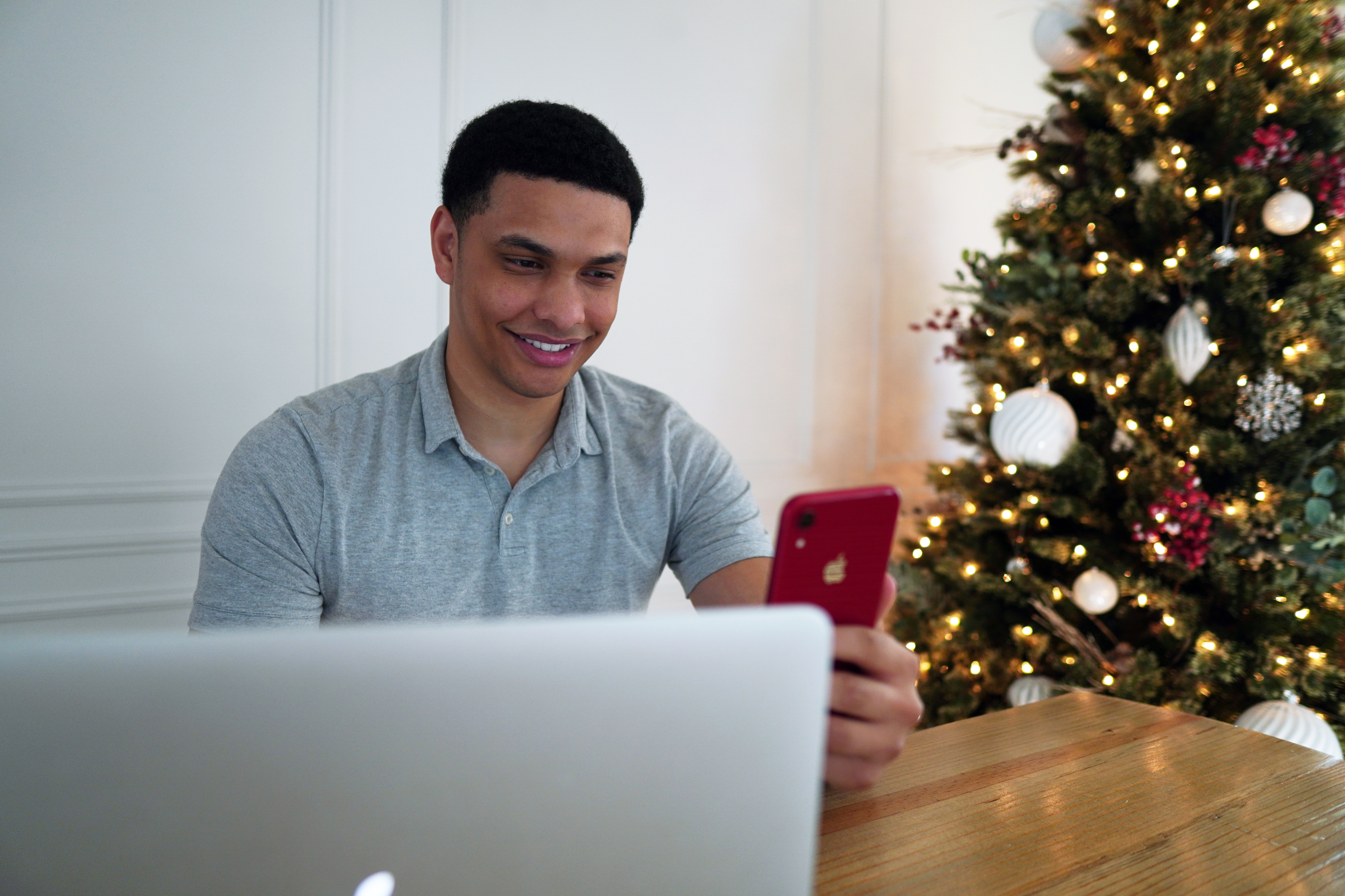 A gentleman taps on his phone next to a Christmas tree