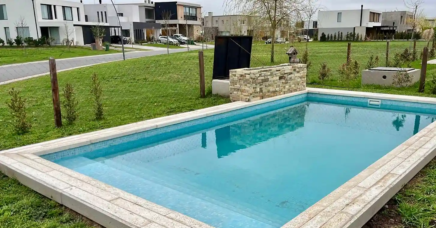 Pileta rectangular revestida en venecitas celestes con amplio escalón de ingreso, ubicada en el jardín abierto de un barrio privado.