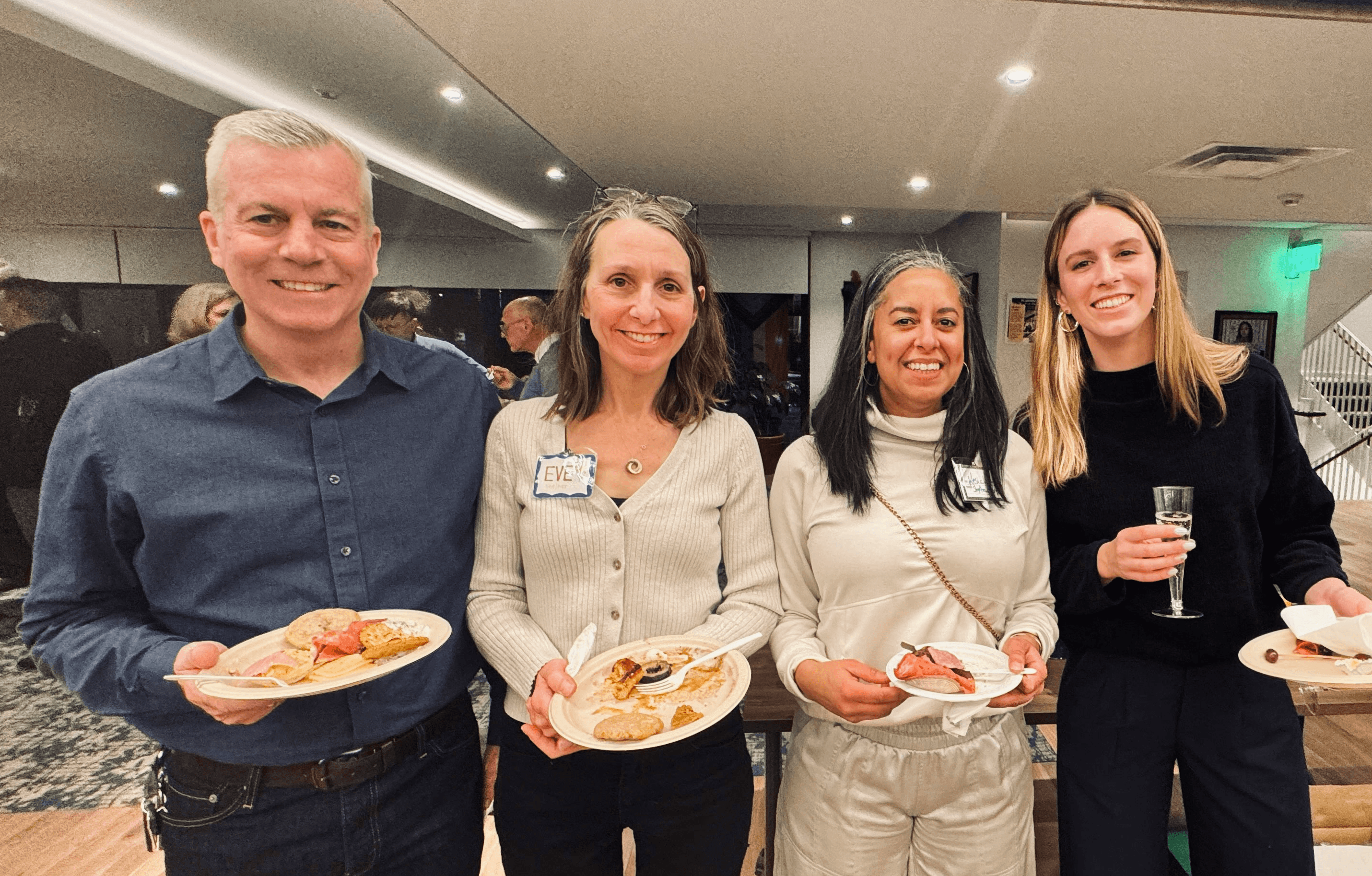 Four Grace Trinity Church members holding plates of food, smiling during a social event.