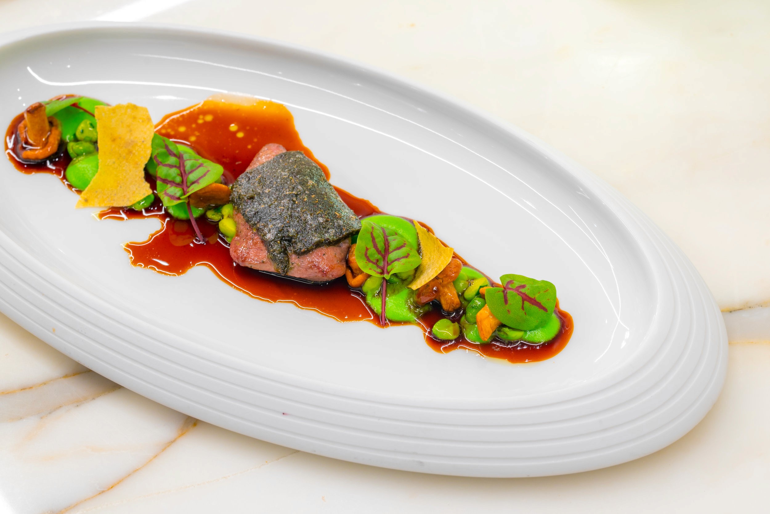 A plated gourmet dish featuring seared tuna with a dark crust, avocado slices, and microgreens on a white plate.