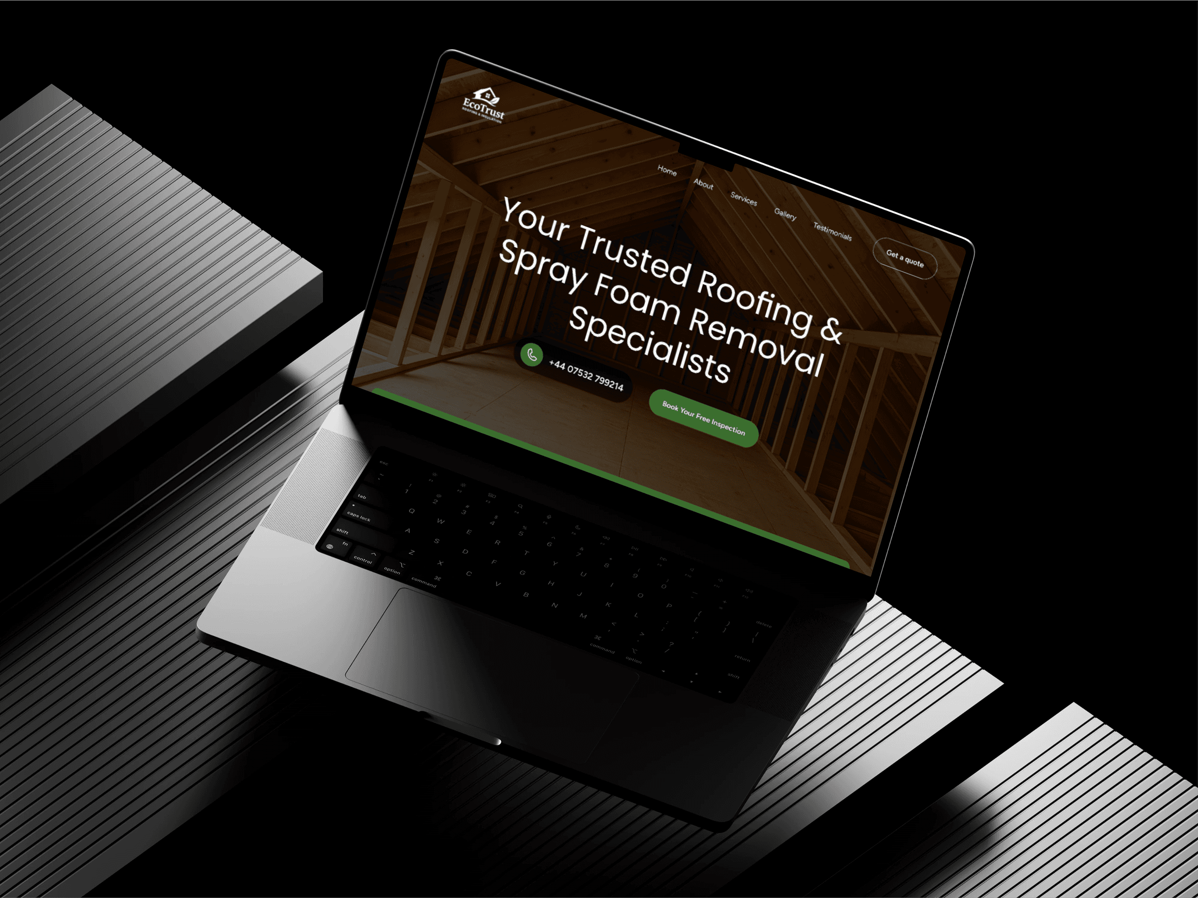 A sleek laptop on a ribbed black surface displays a website homepage featuring a roofing and spray foam removal service, with a warm wooden interior background and green call-to-action buttons.