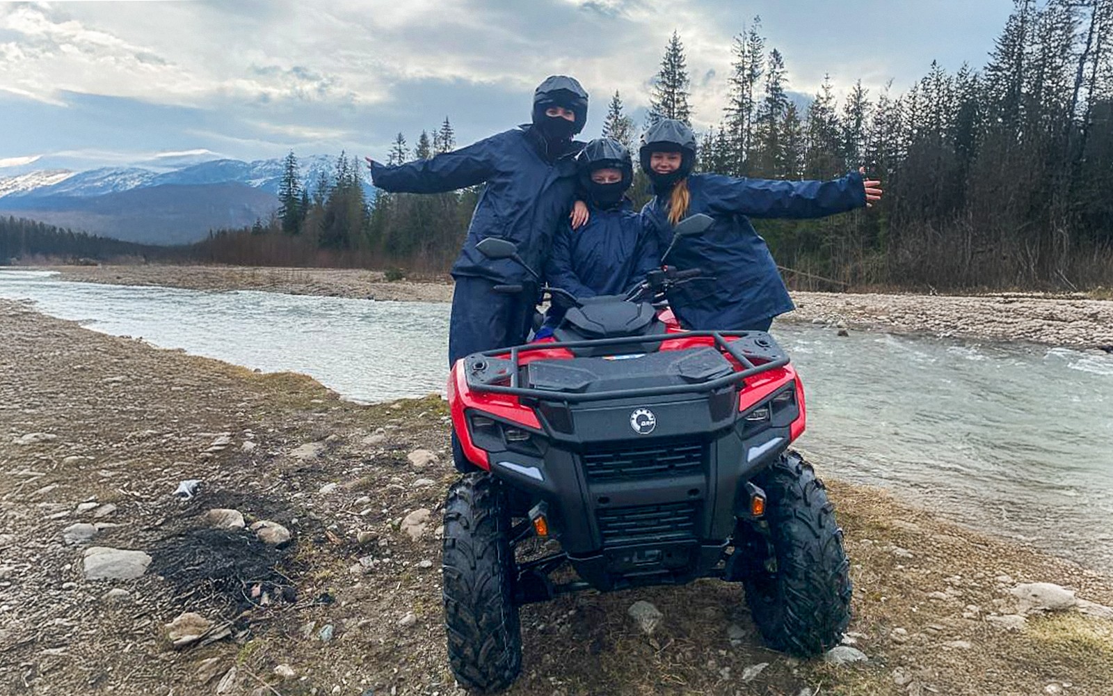 Visitors on a quad bike by a river in Zakopane, Poland, with mountains in the background.
