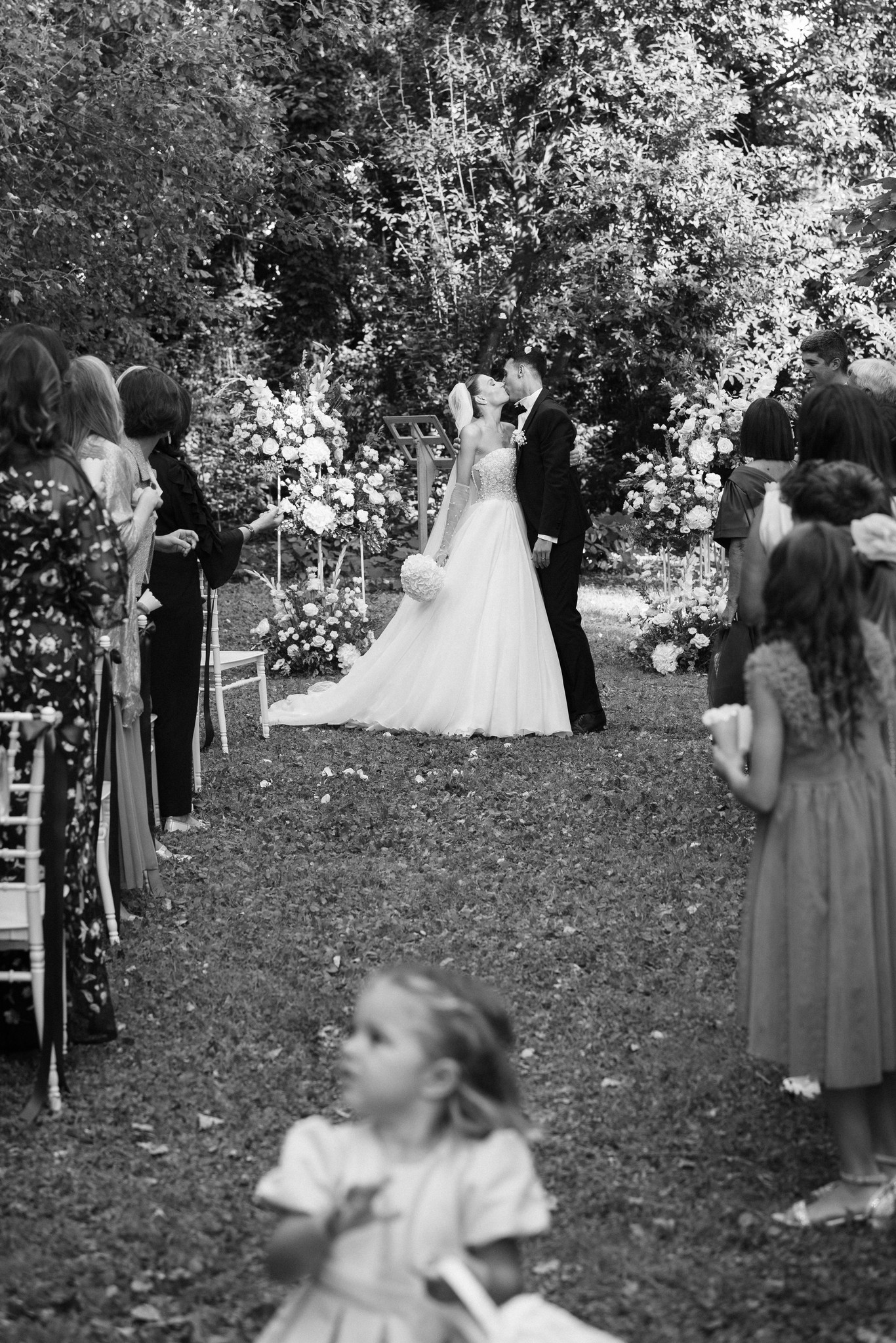 Cerimonia matrimoniale nel parco di Villa Ferrari, sposi sotto il pergolato fiorito circondati da ospiti, reportage Fotolize