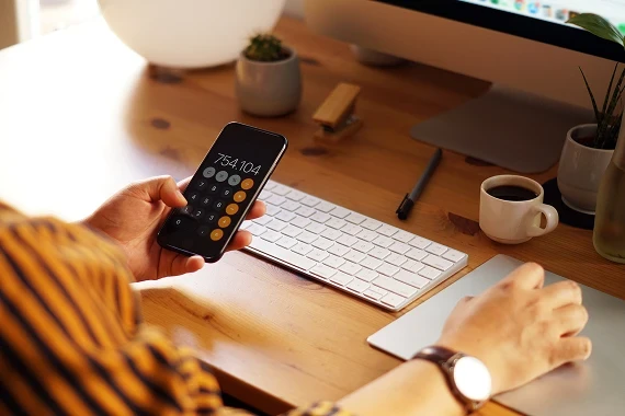 Over-the-shoulder shot of someone at a home office desk using a calculator app to budget for interior design.