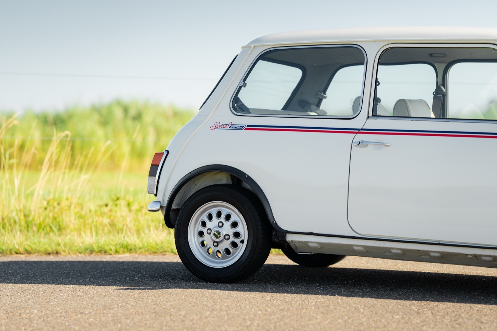 A close-up of a white vintage vehicle parked on a road, with green fields in the background.