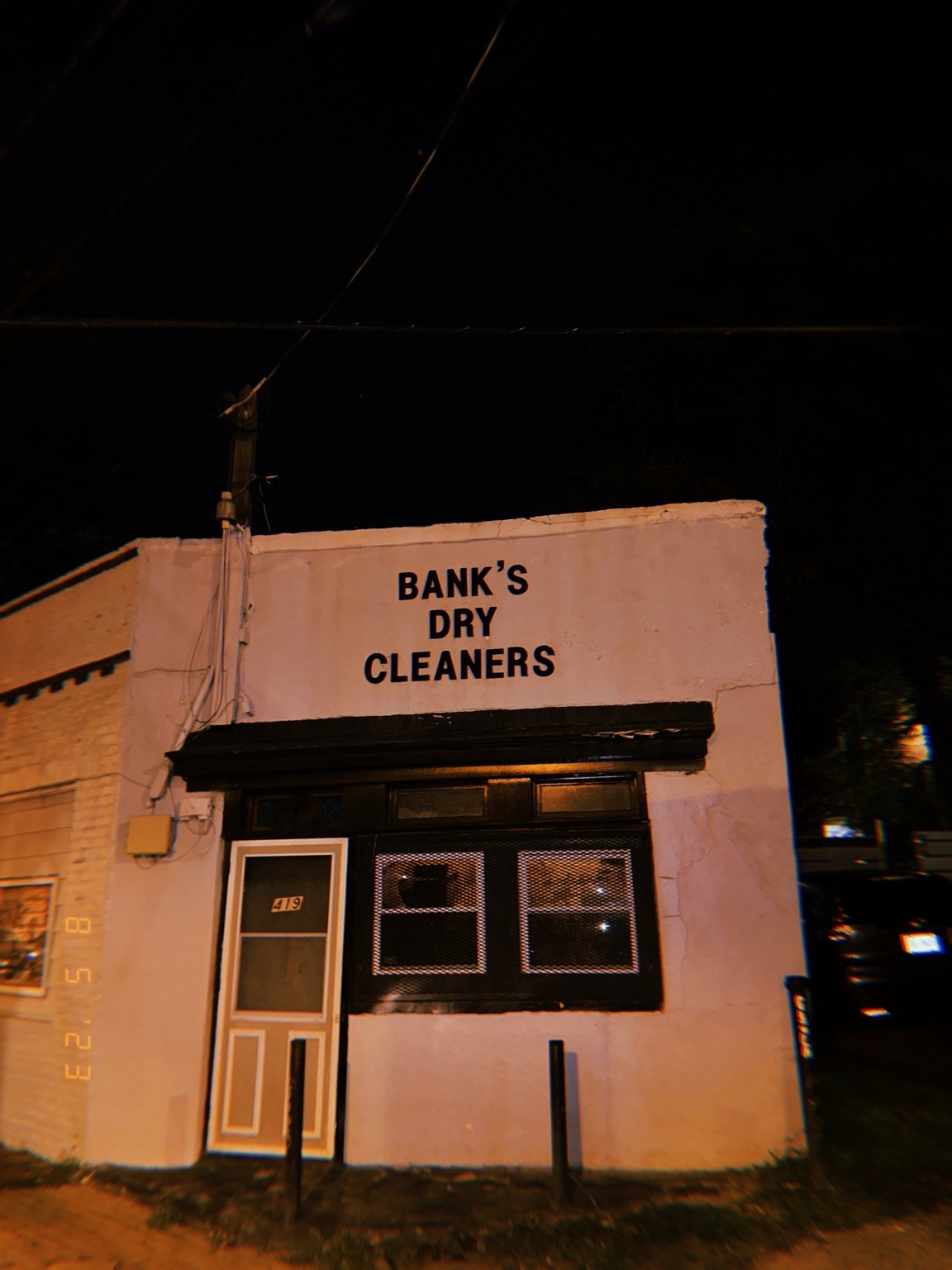 Bank’s Dry Cleaners on a pale storefront illuminated at night.