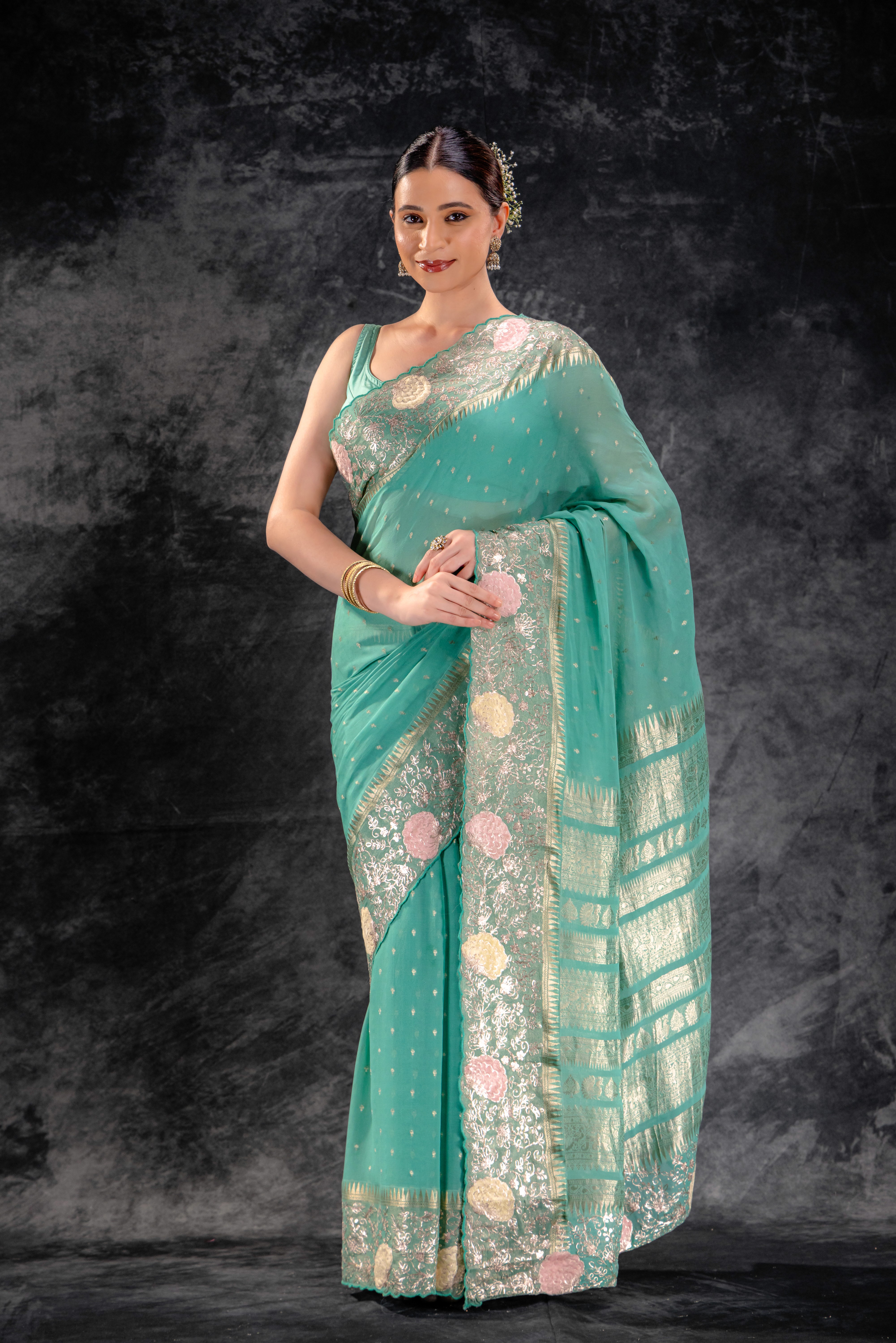 Woman wearing a teal saree with floral patterns against a dark background