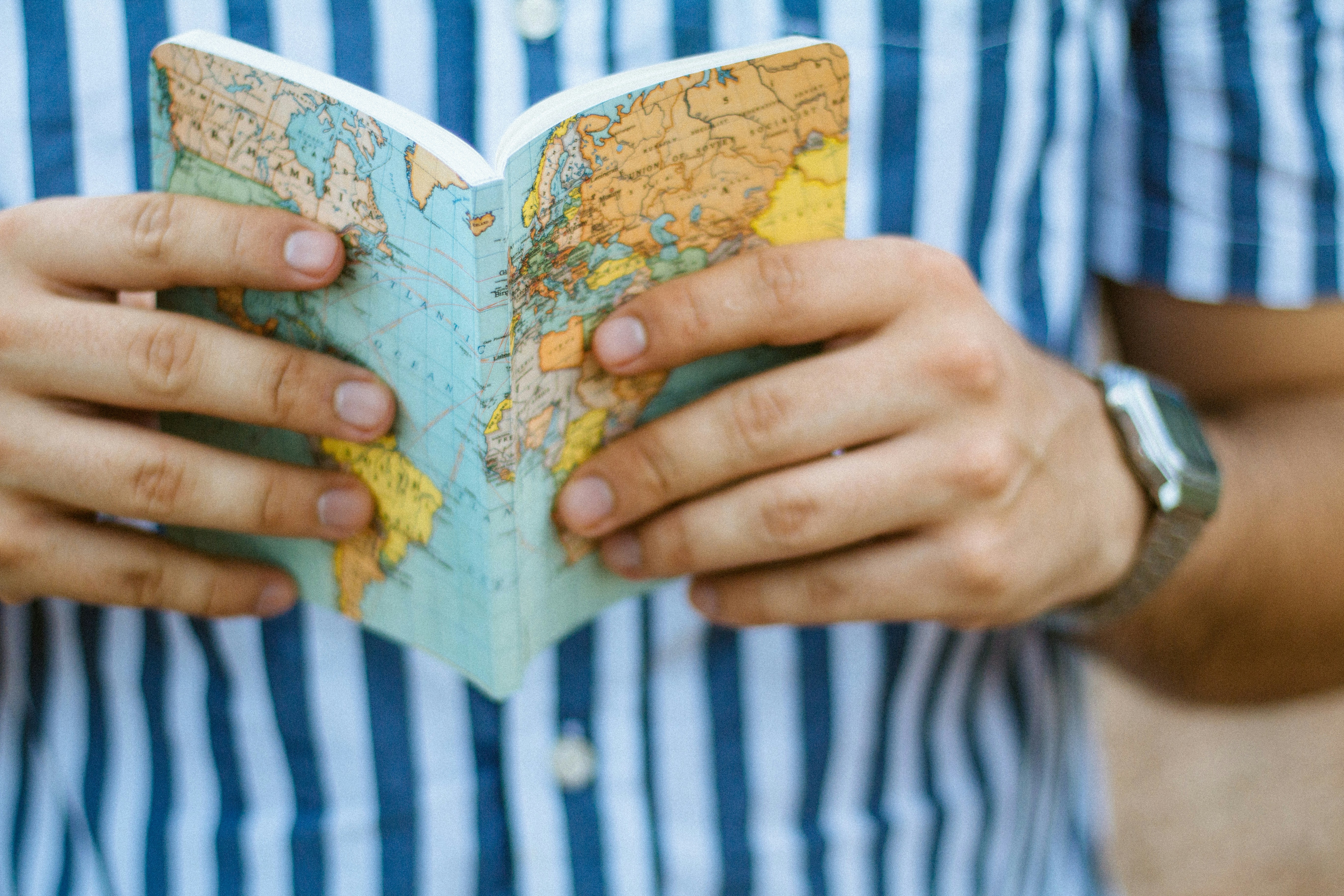 Person holding an open notebook with a world map cover, symbolizing the importance of a clear guide to navigate and maintain a consistent brand voice across all content platforms.