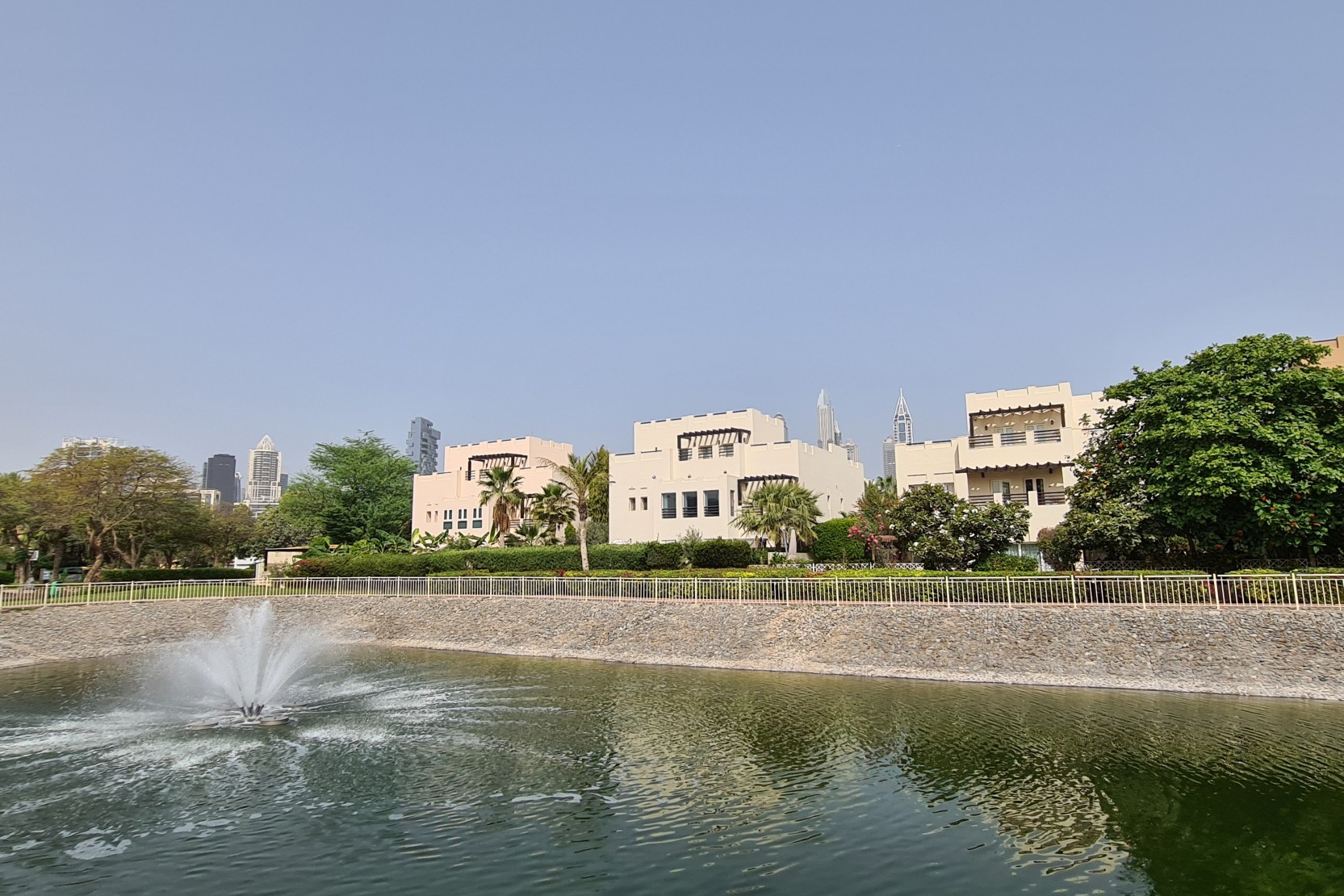 A fountain in front of Hattan 1 buildings, with a large structure visible in the background.