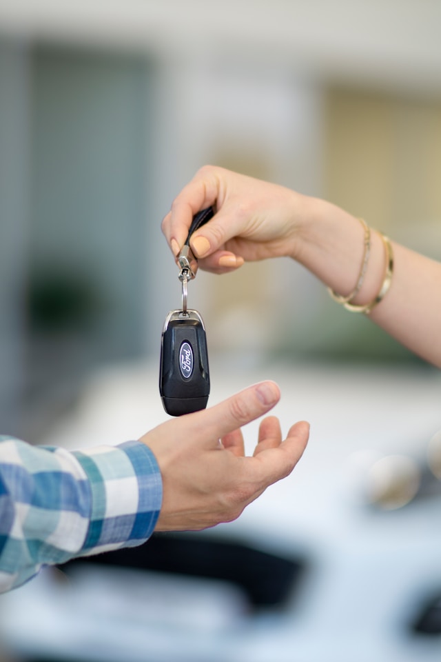Person handing car keys to another, symbolizing the start of a car rental or car lease agreement.