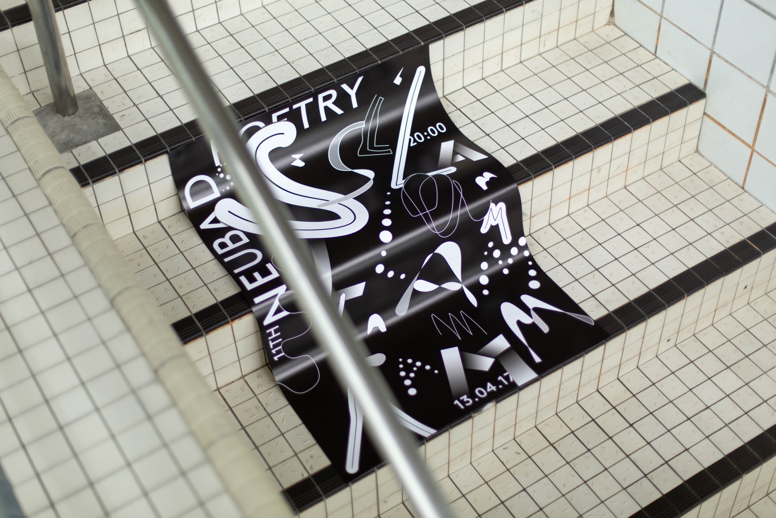 An expressive poster design with bold, playful typography set in black and white, laying on a tiled pool floor.