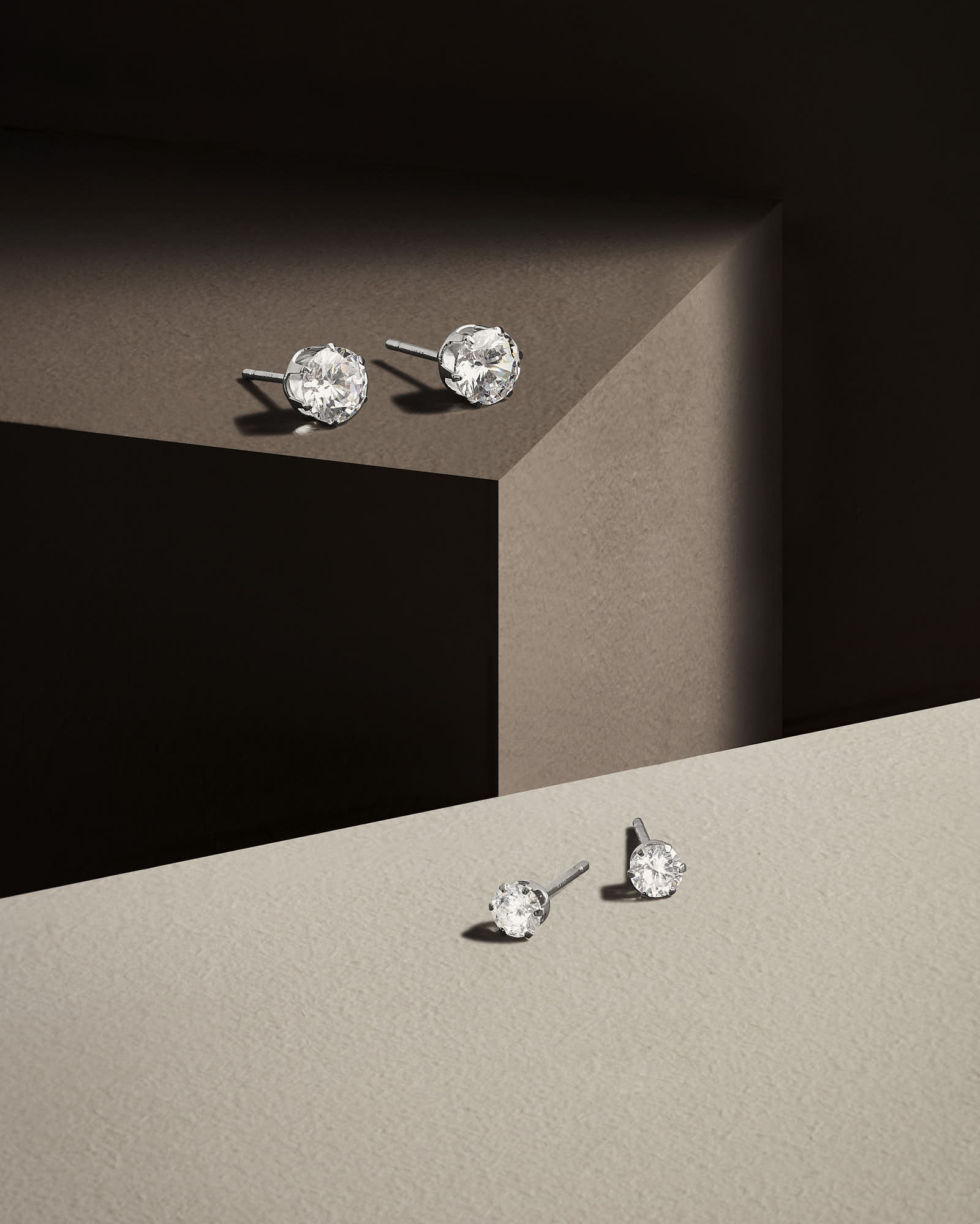 Close-up of two earrings displayed on a minimalist surface with geometric shapes and soft lighting.