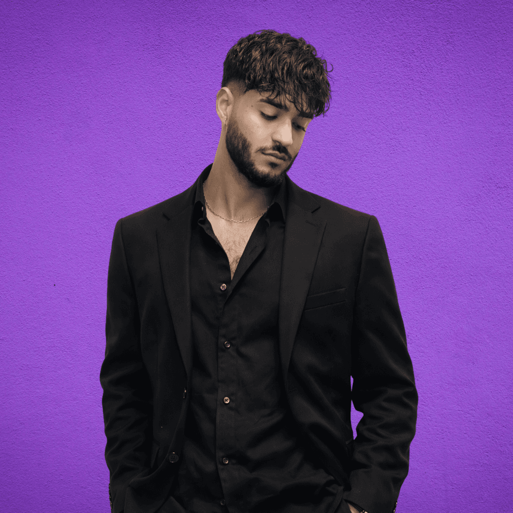 a man looking away from the camera in a black suit and black buttoned shirt