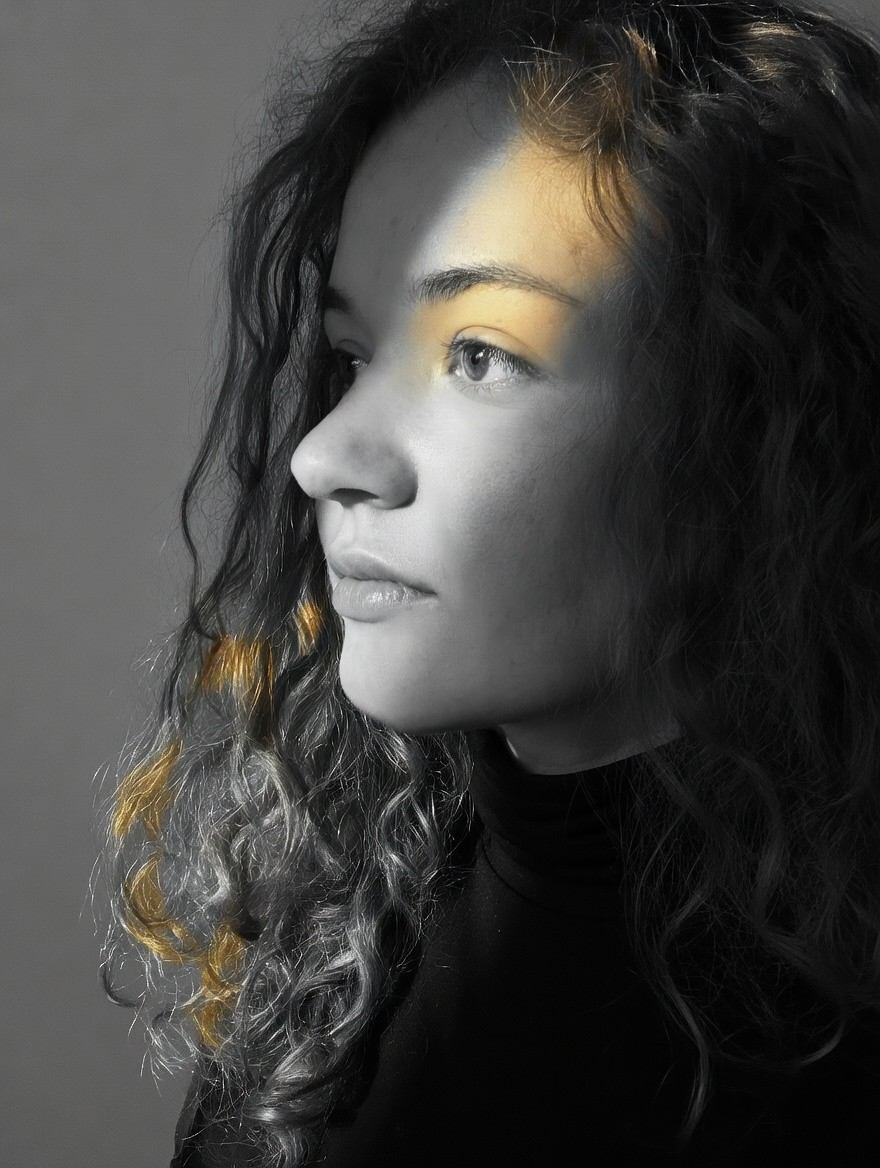 Artistic portrait of a man wearing glasses, illuminated by a diagonal streak of light against a gray background.