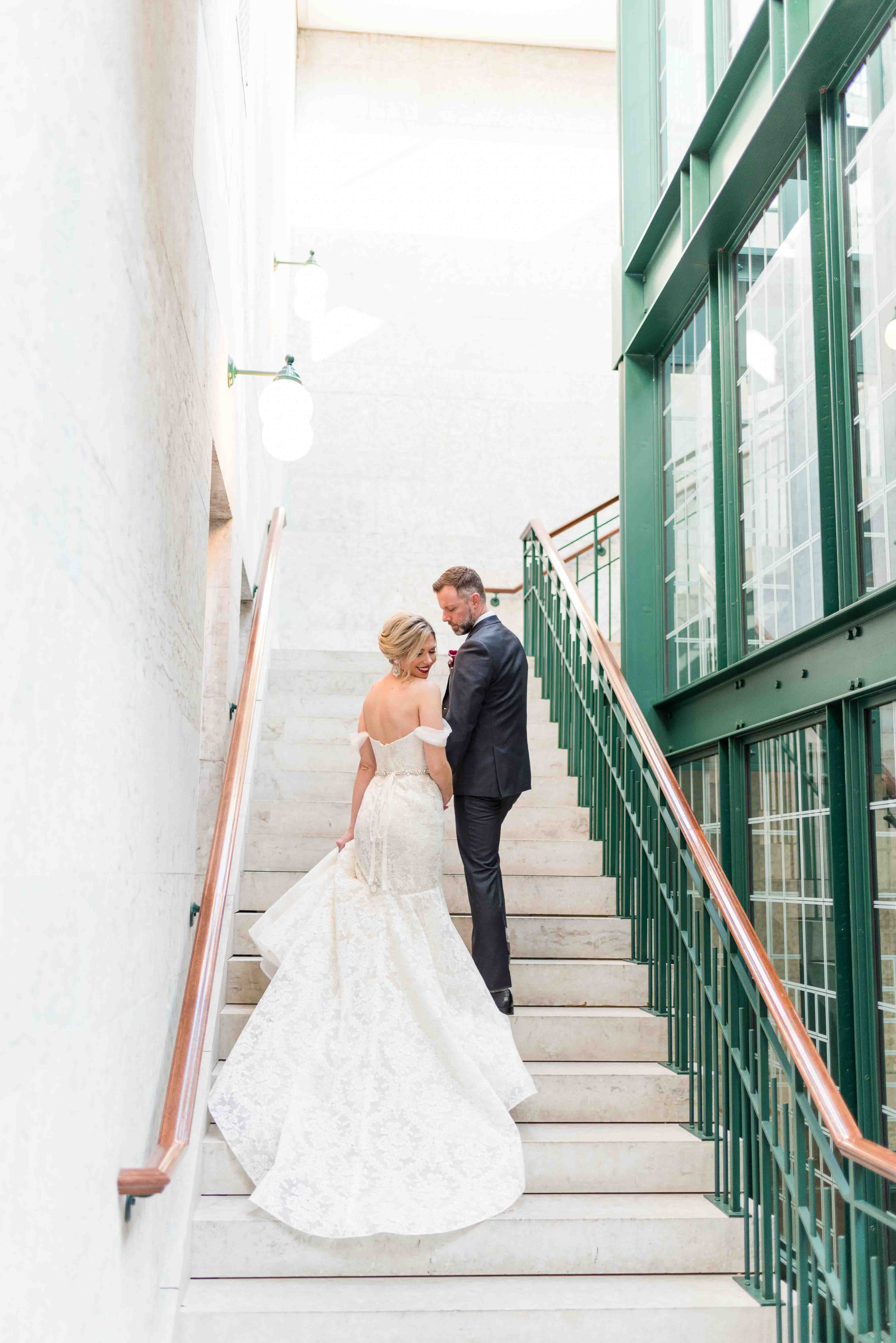 Bride and groom walking up the stairs on their wedding day with her dress cascading down the steps.