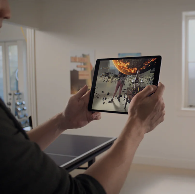 Person using iPad for augmented reality AR experience showing interactive holographic planet overlay in home environment