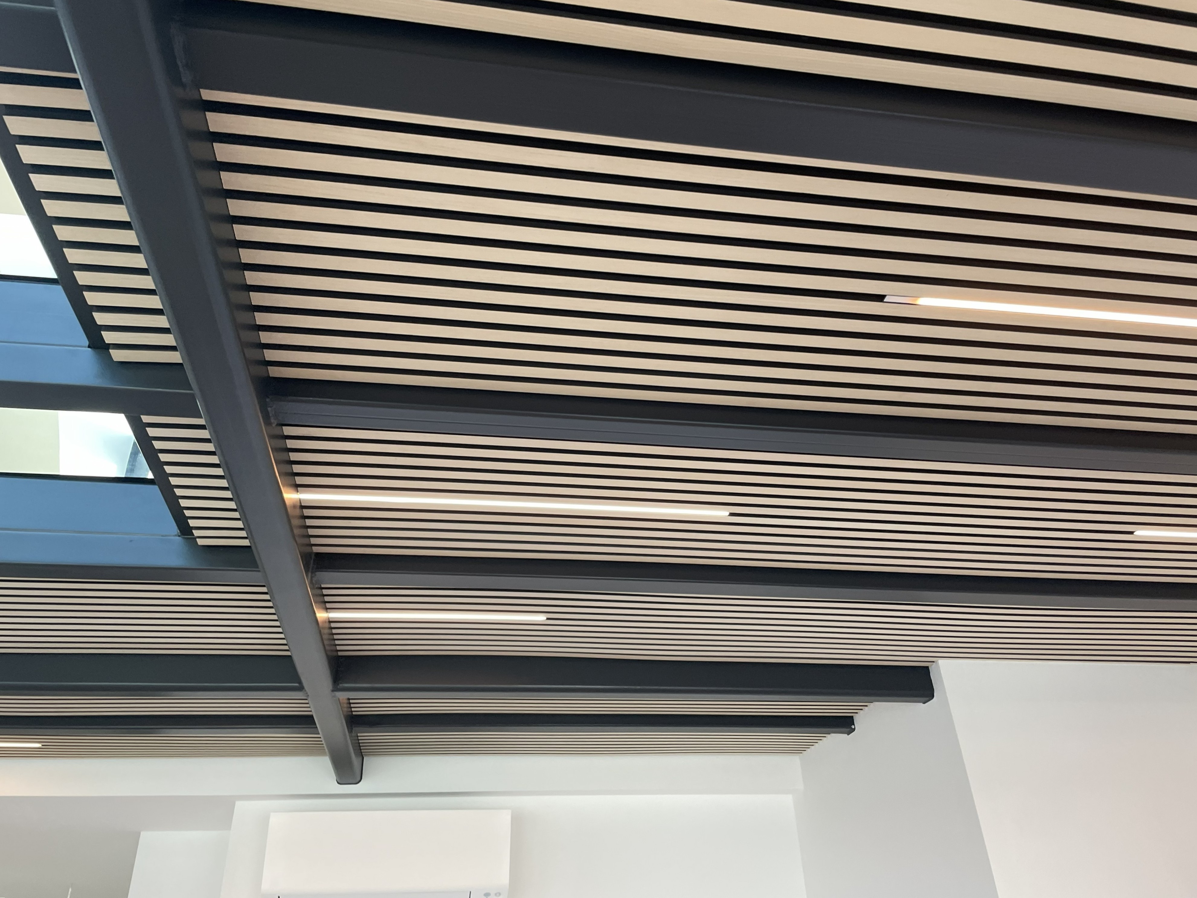 Detailaufnahme der Akustikdecke mit Holzlamellen und Stahlträgern im Dachausbau.