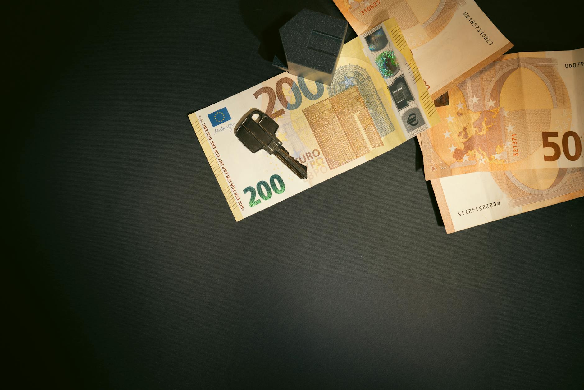 Euro banknotes and a property key with a miniature house model on a dark background