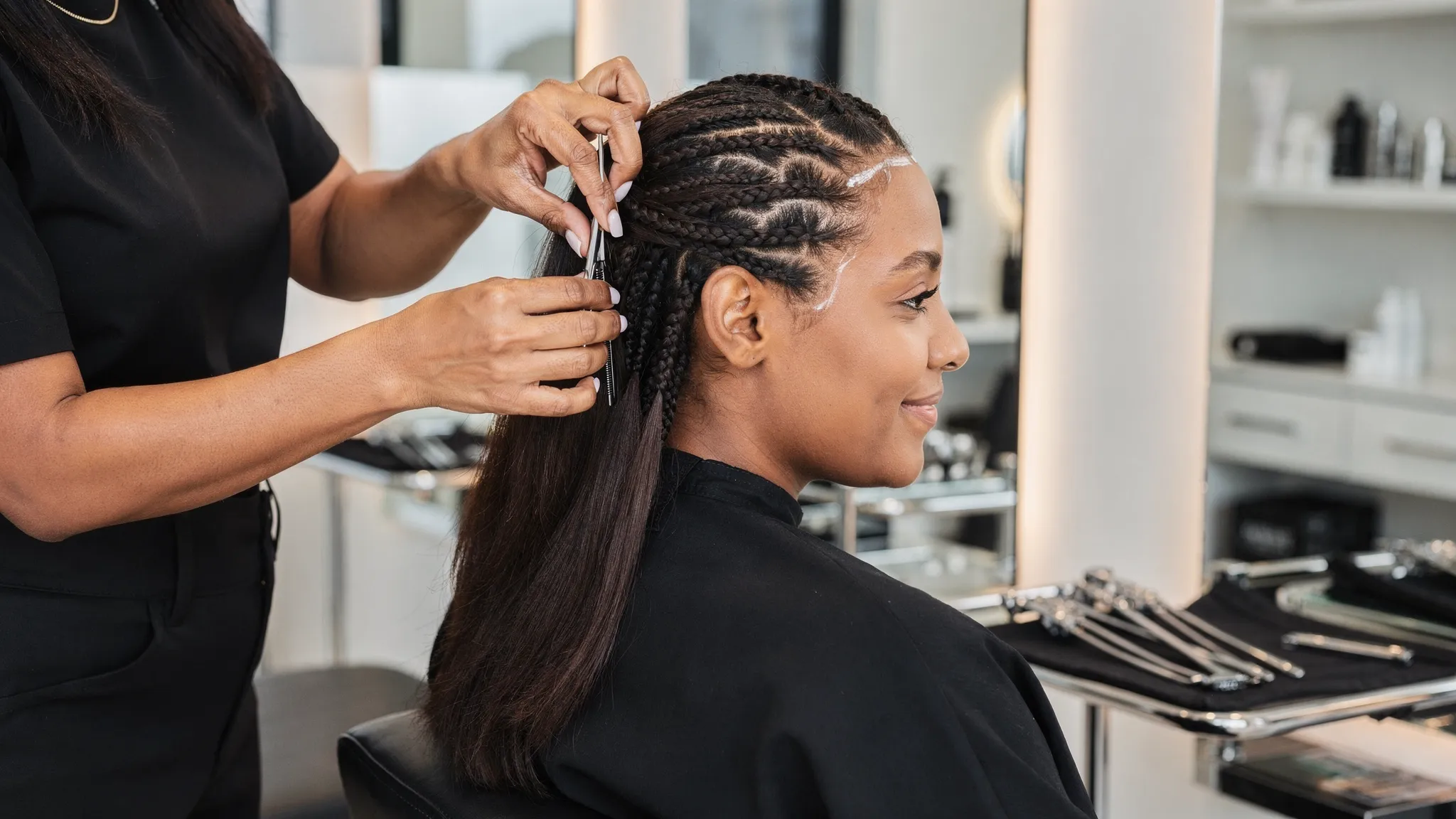 A stylist gently sectioning textured hair for neat protective braids in a clean upscale salon while the client sits comfortably with healthy edges protected.