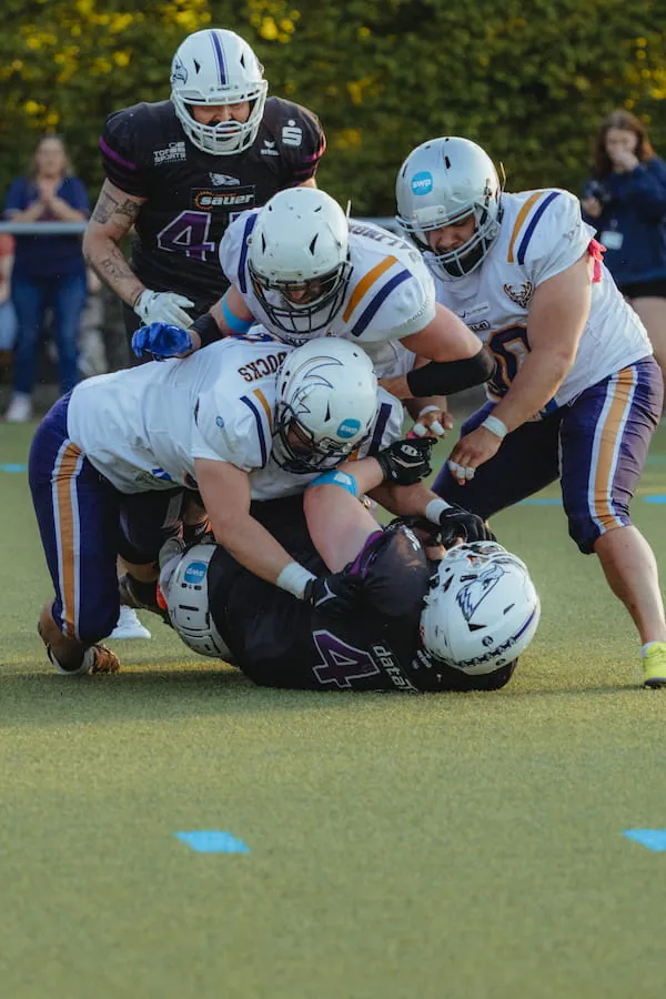 Mehrere Spieler der Bucks in Weiß bringen einen Gegner beim Tackle gemeinsam zu Boden.