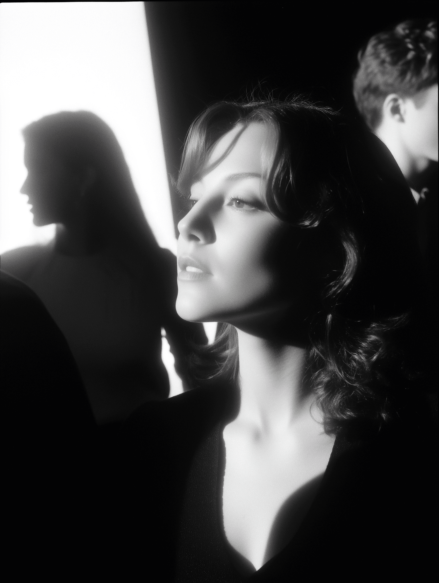 Woman in black top with strong side lighting and blurred figures behind