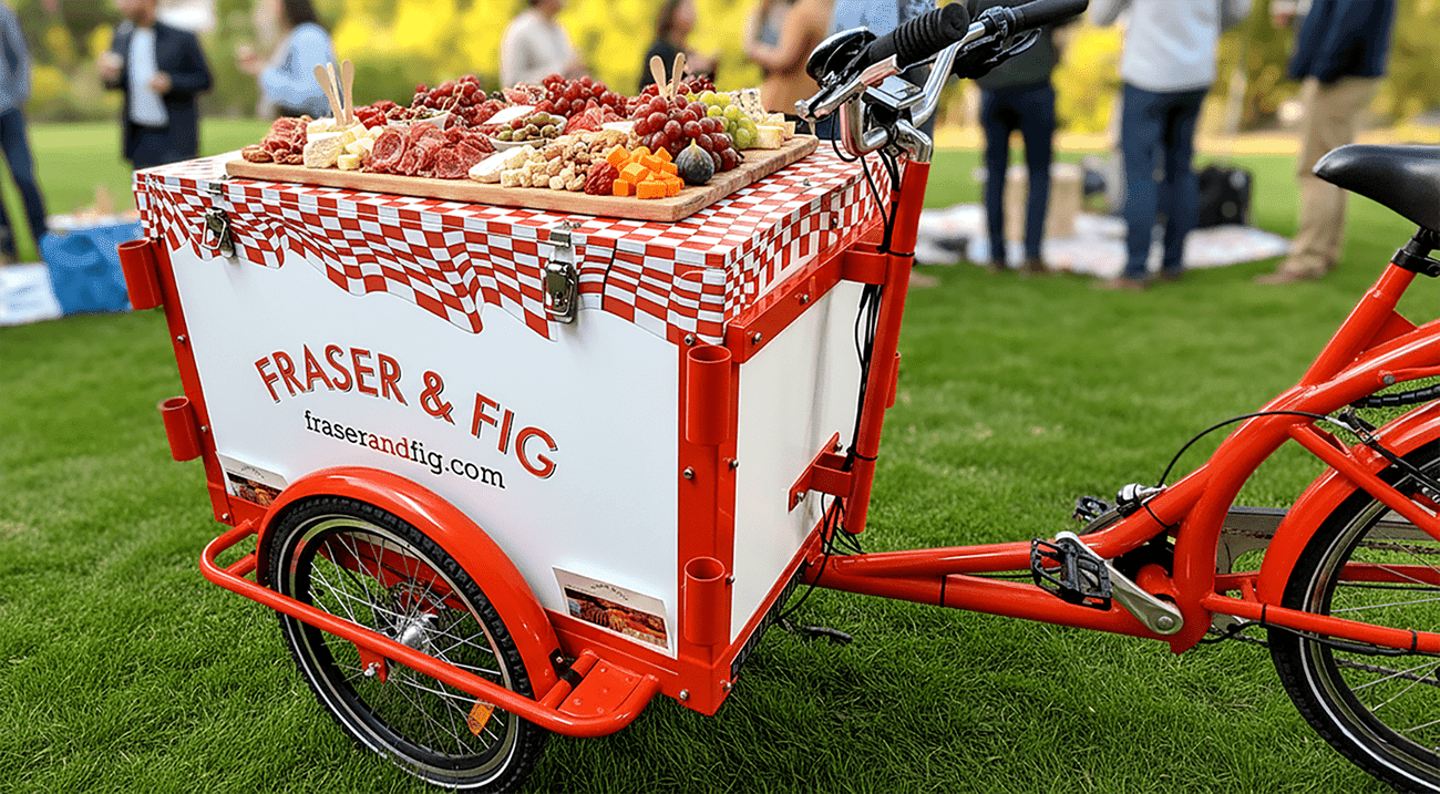 a red-and-white bicycle with fridge box attachment and vinyl wrap on top, reading Fig & Fraser on the sides and front