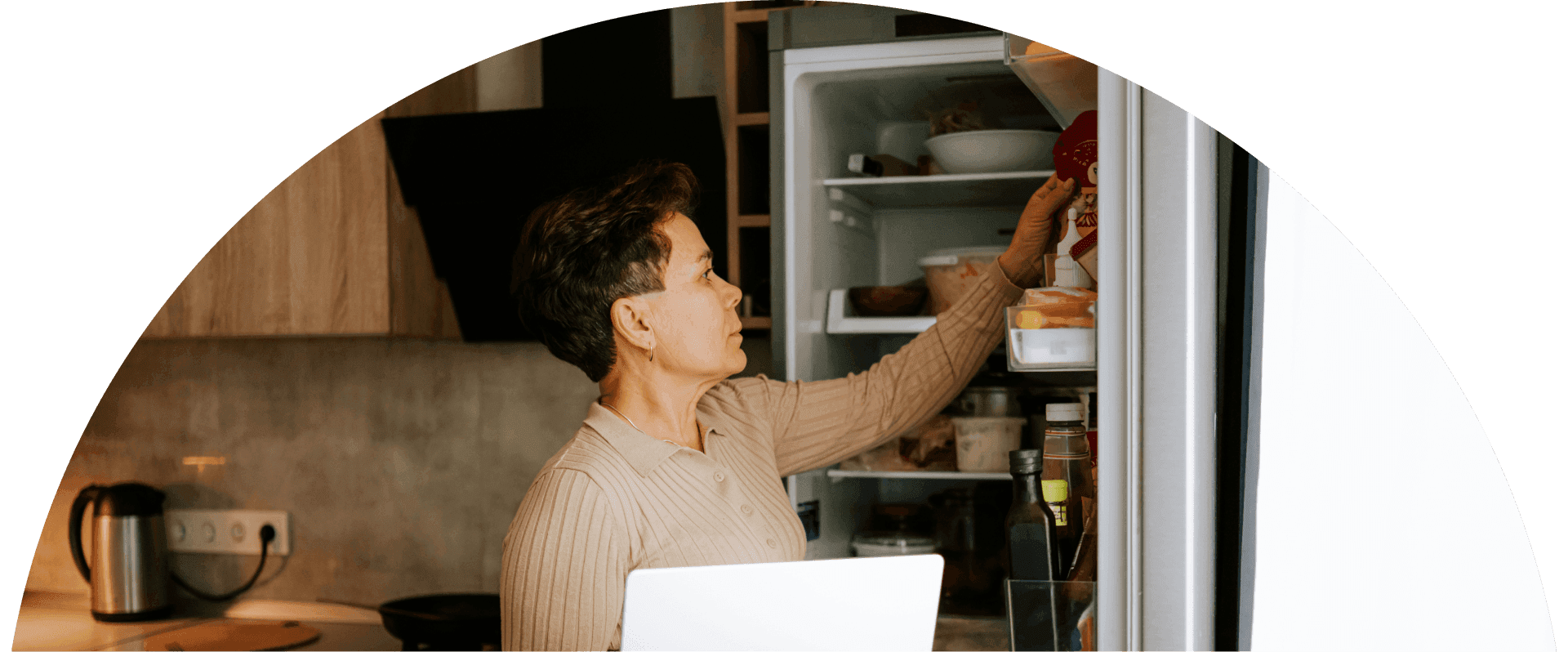 Woman stands in a modern kitchen reaching into an open refrigerator to grab ingredients
