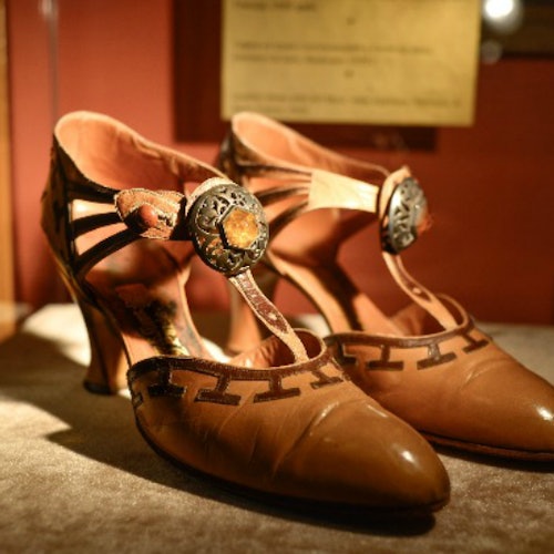 一双复古棕色皮革高跟鞋，鞋面带有复杂的绑带和华丽的扣子，陈列在柔软的表面上。