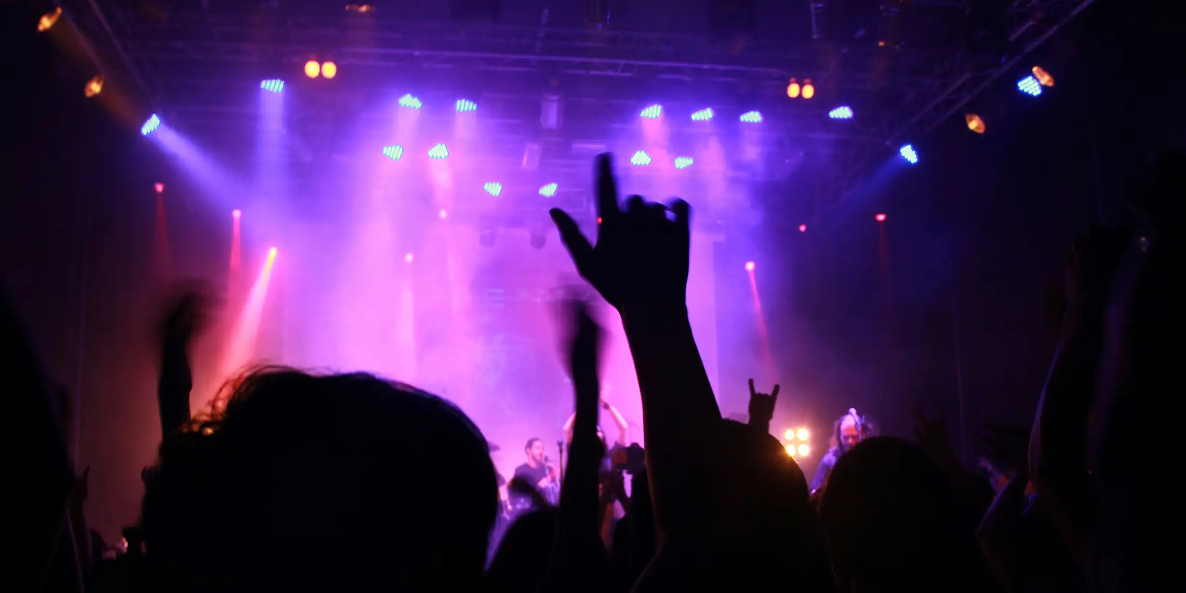 Silhouette of a raised hand at a live music event, lit by warm stage lights, representing shared experience and collective energy