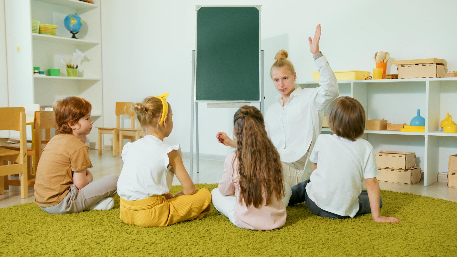 A teacher kneeling beside a small group of students to facilitate a collaborative play and learning activity.