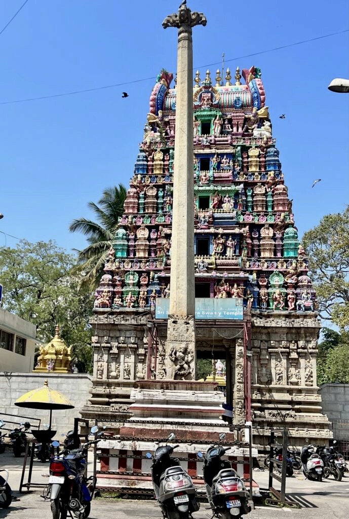 Dhwajstambh of Halasuru Someshwara temple. A few scooters are parked at the entrance of the temple.
