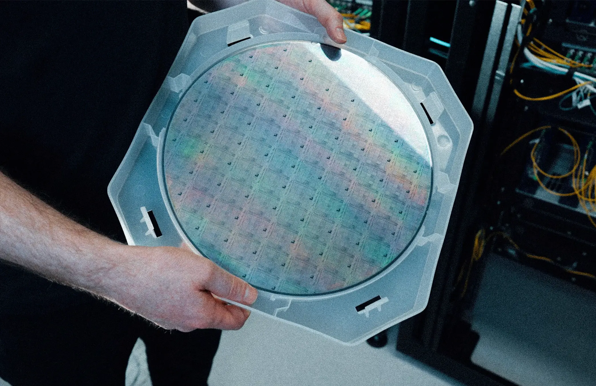 Technician holds a glowing transparent tablet with a grid-like interface while server racks and cables blur behind, supporting tech marketing strategy.