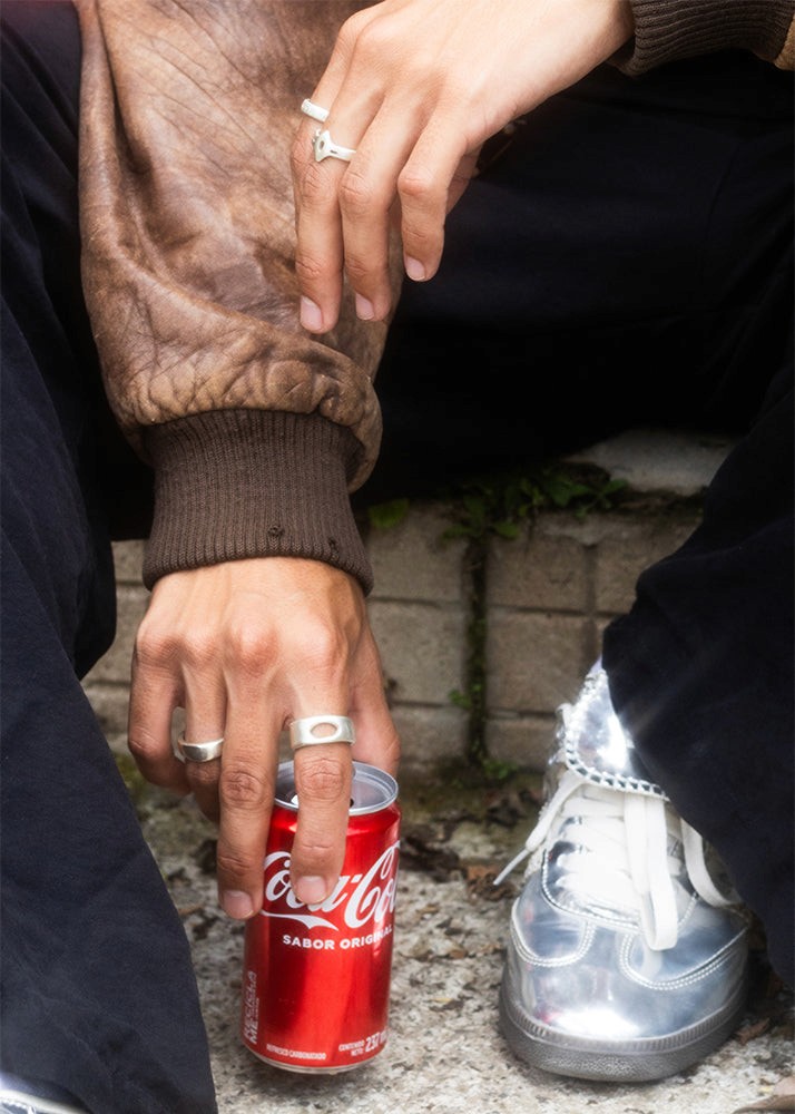 Person holding a Coca-Cola can with silver rings on a stone surface
