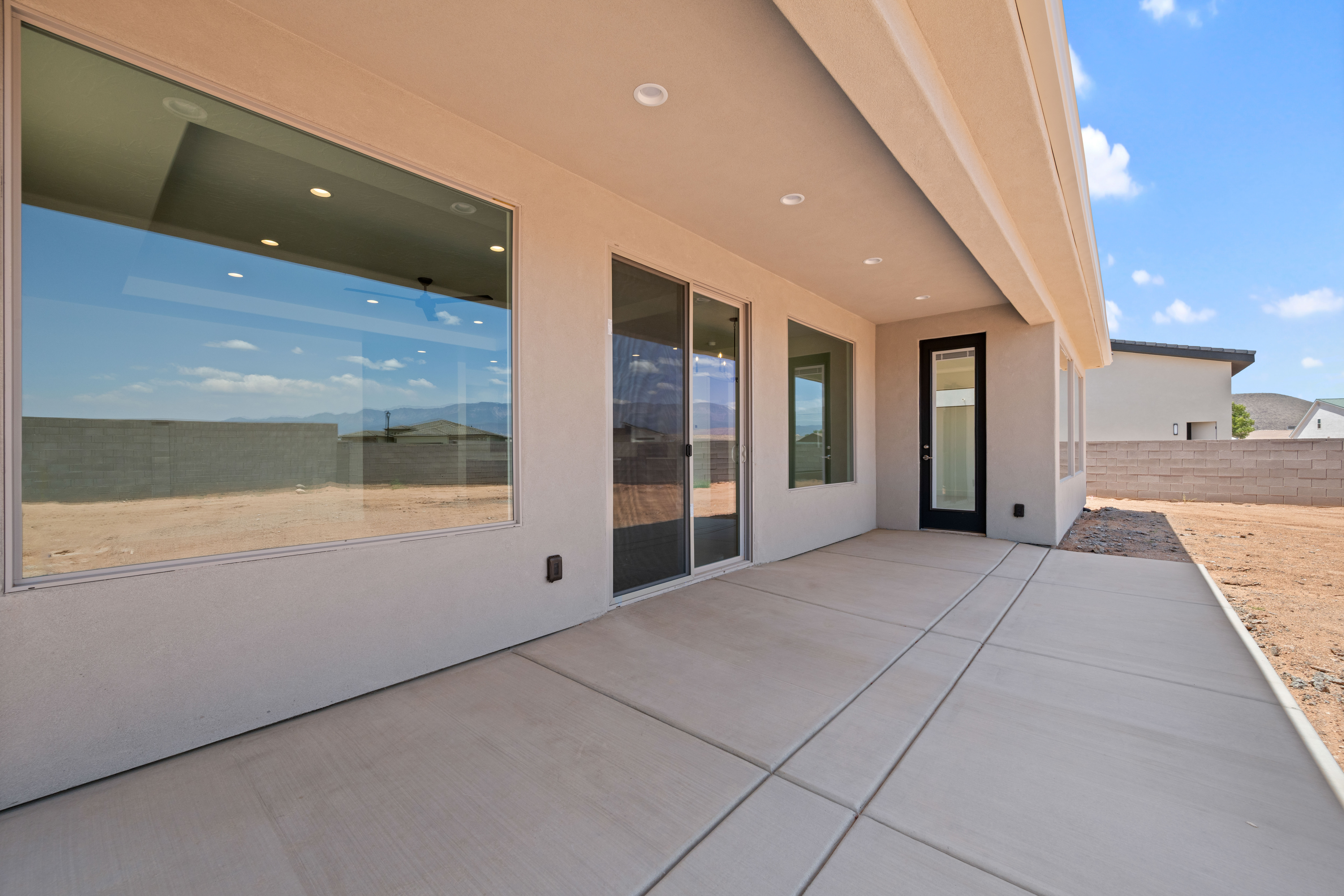 Rear exterior of The Nest at Falcon Ridge in Hurricane, Utah, featuring a concrete patio, stucco walls, and large windows and sliding doors that open to the backyard.