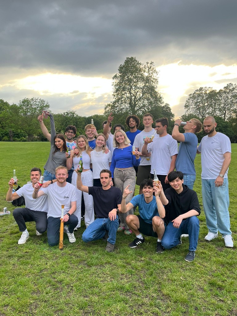 A group of people posing together in a park under a cloudy sky, smiling and enjoying their time outdoors.