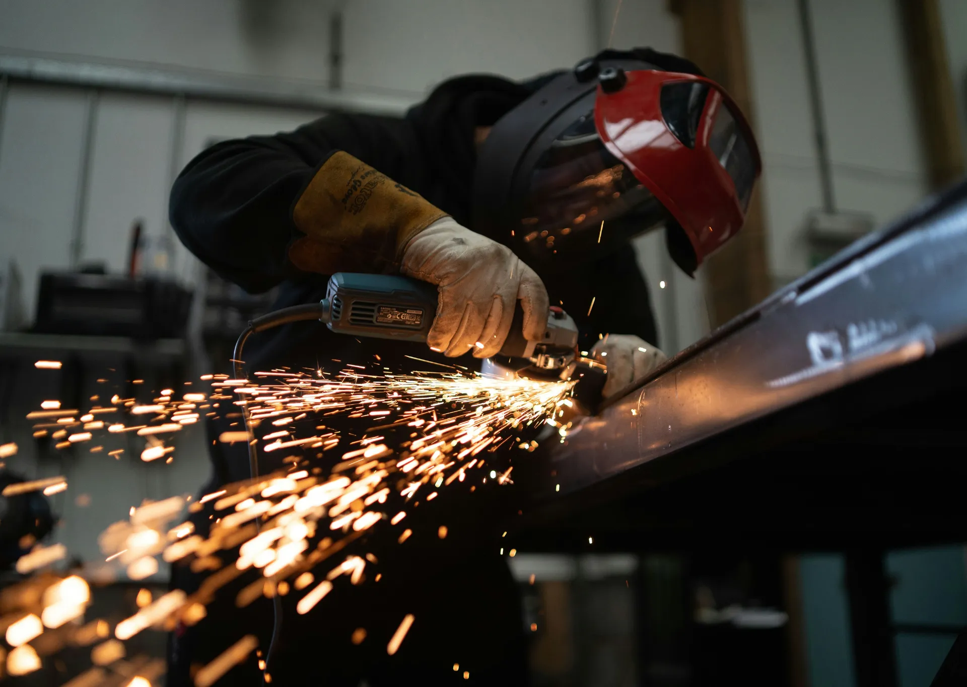 Steel fabrication process with worker grinding structural beam, producing sparks during metal finishing operation