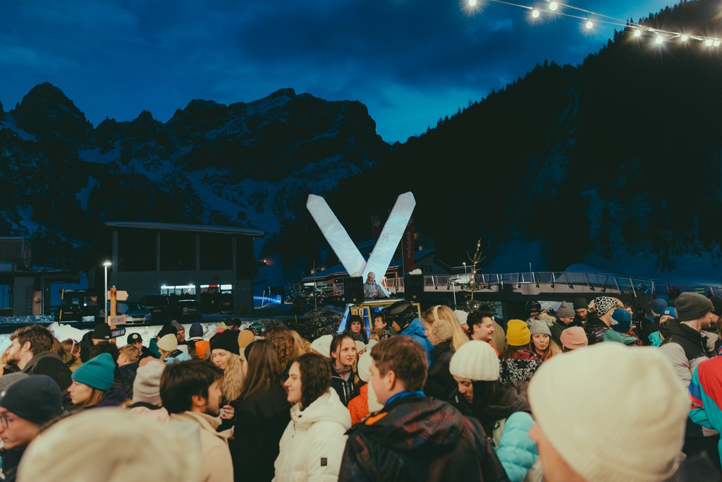 Crowd enjoying outdoor winter event with mountains and lights at night.