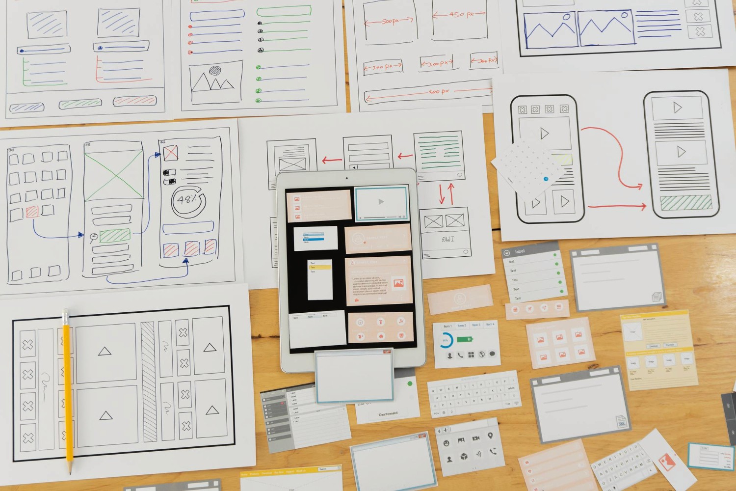 Mehrere gezeichnete und beschriftete Wireframes und Mockups für eine App oder Webseite auf einem Holztisch verteilt