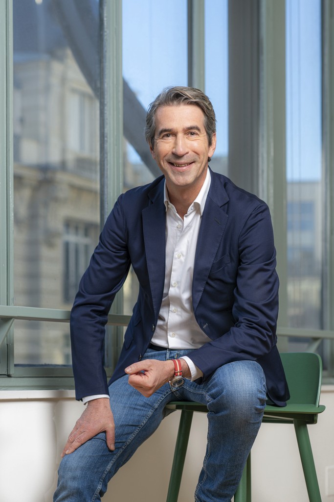 A person with wavy, shoulder-length hair wears a cream beanie and a matching thick-knit sweater over a gray shirt, giving a cozy, relaxed vibe.